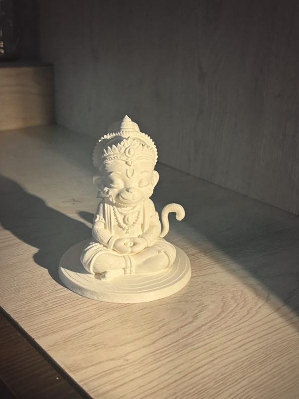 3D printed white Hanuman idol in meditation pose on a wooden shelf